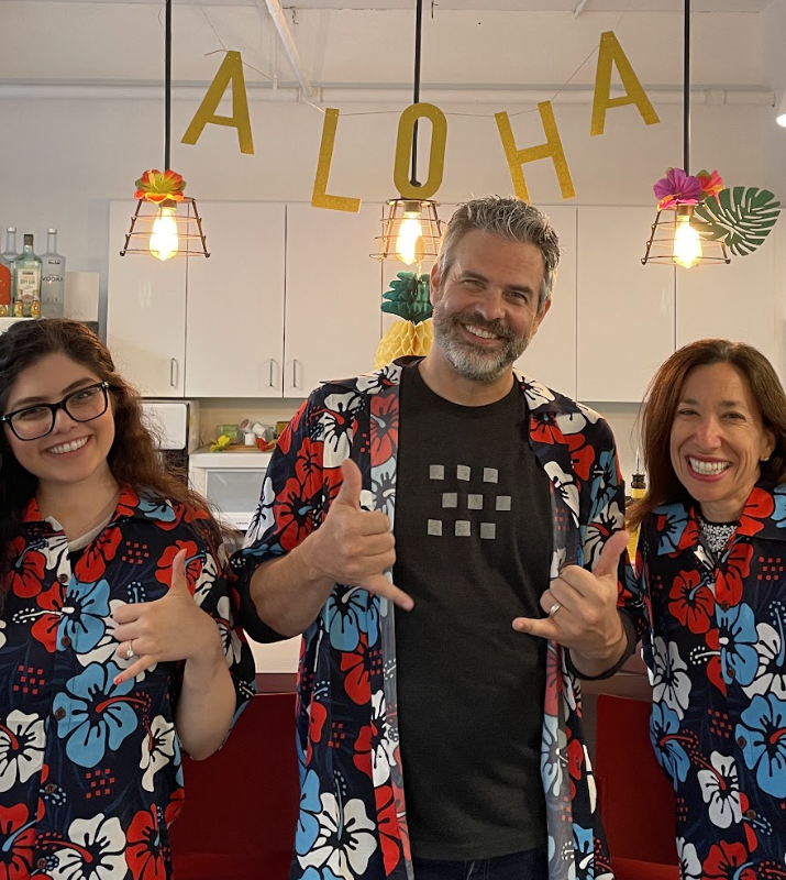 Three employees wear custom Hawaiian shirts with 'hang ten' sign