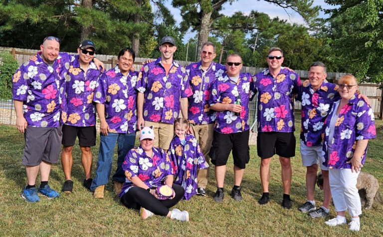 A photo of eleven people (and one dog) outside wearing purple Hawaiian shirts.