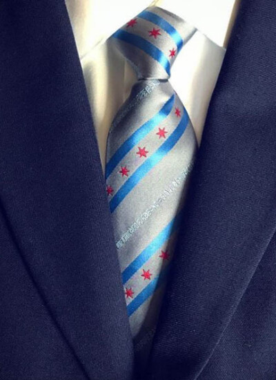 We created these ties for the <a href="http://chicagopipeband.com/" target="_blank" rel="noopener">City of Chicago Pipe Band</a> based on their design by their tenor drummer Grace Keppel. They noted, "It is our first totally custom uniform item since the band was founded and we were glad to be able to work with a Chicago-based company and an in-house design!" <br /> <br />Photo credit: ChicagoPipeBand on Instagram. Closeup of a tie and vest. The tie is silver with the Chicago stars and stripes, with the text "Chicago Pipe Band,"